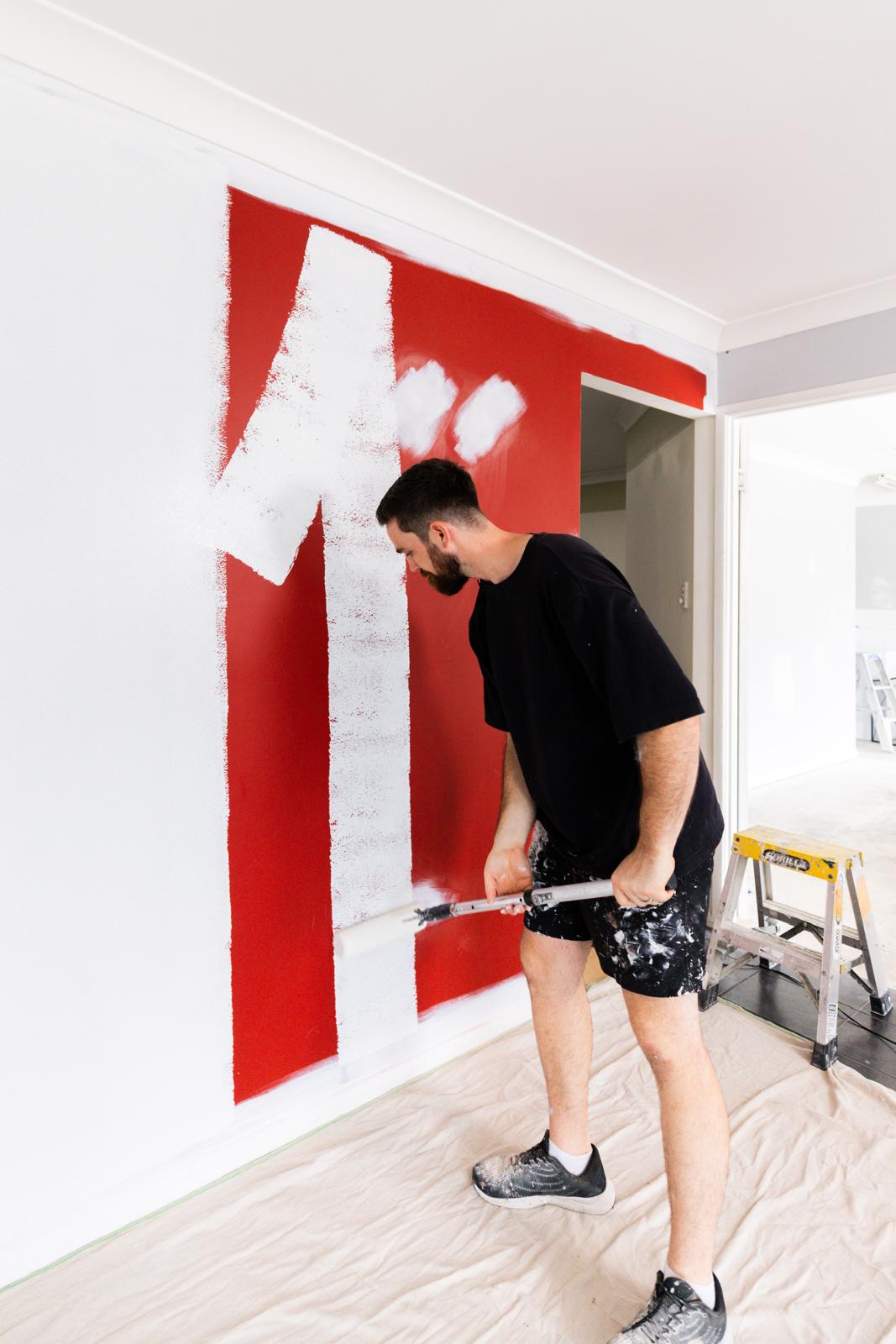 Rolling white primer over red feature wall during a residential repaint south-east Queensland