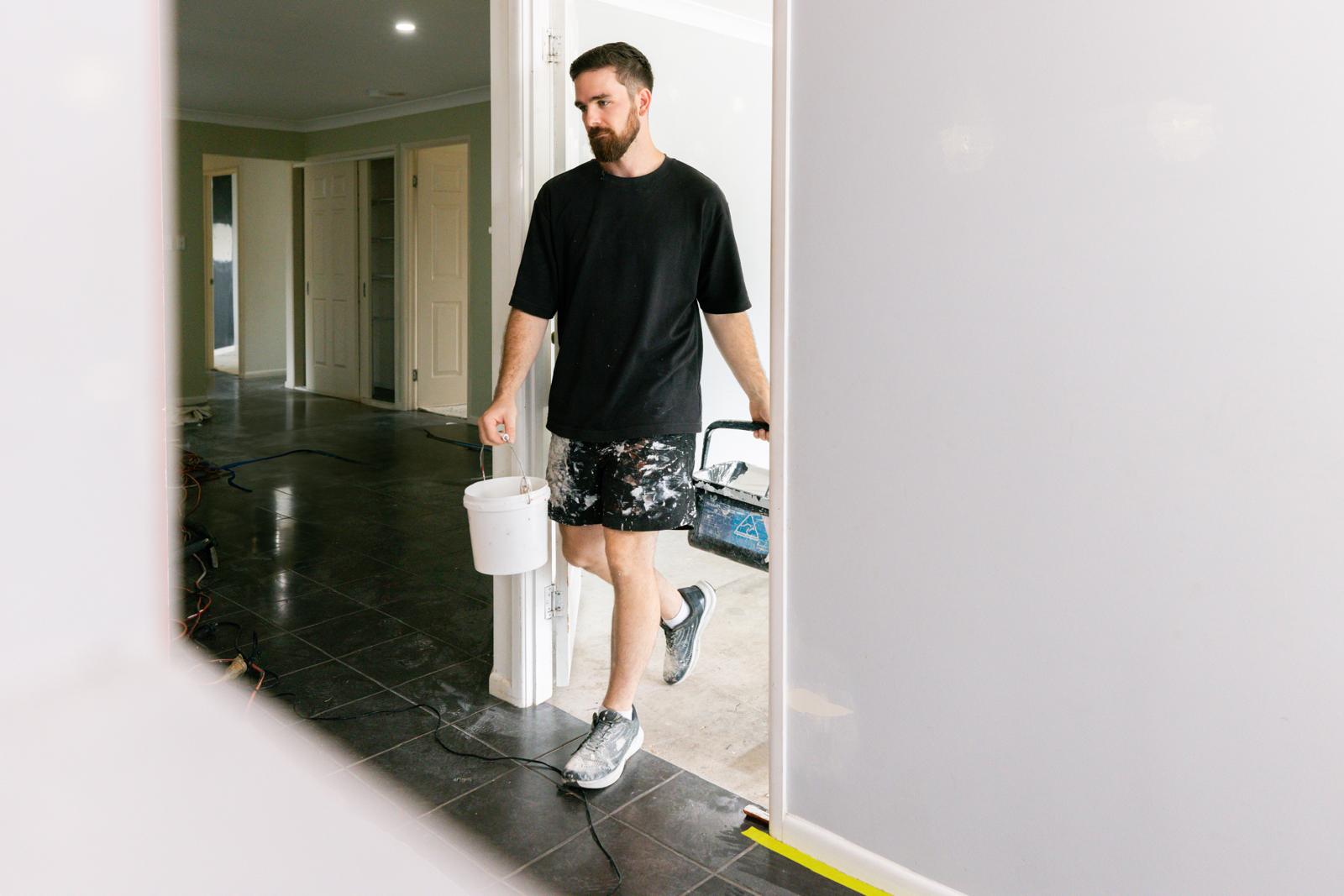Professional painter carrying supplies through freshly painted interior doorway in a south-east Queensland home